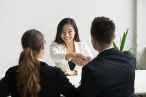 Happy millennial female applicant getting hired and shaking HR Director's hand.