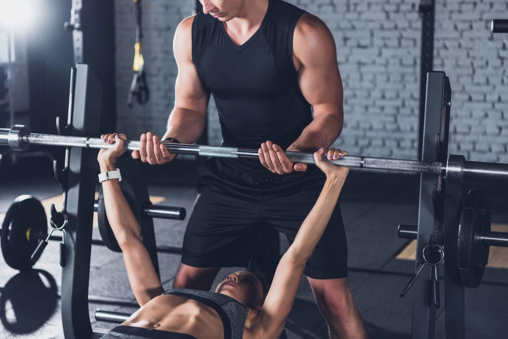 Fitness trainer helping a client with weightlifting at a gym. © / Adobe Stock