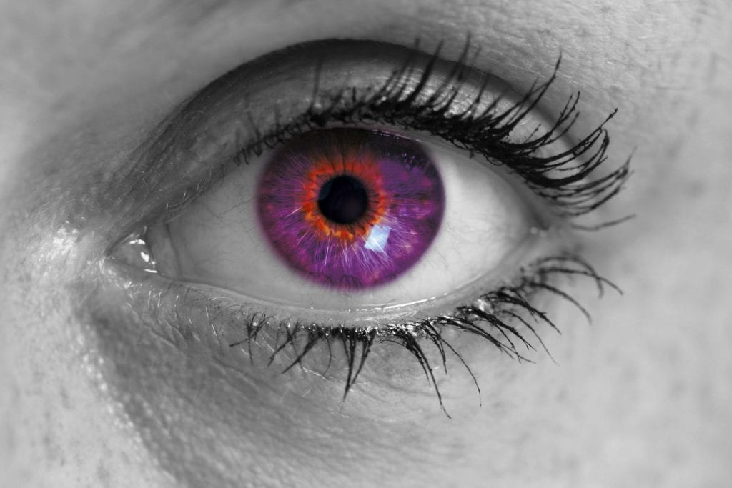 ‎Close-up of an eye with a purple iris and thick, dark lashes.